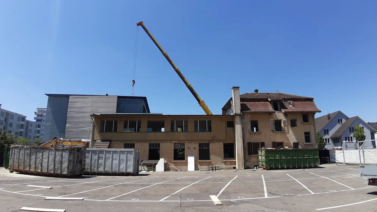 Baustelle mit Abbruchhaus, Schuttmulden und Pneukran im Hintergrund.